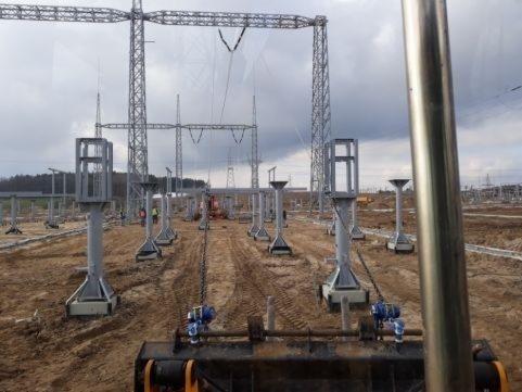 Wykop pod fundamenty słupów wysokiego napięcia, widok z kabiny maszyny budowlanej, w tle konstrukcja linii energetycznej.