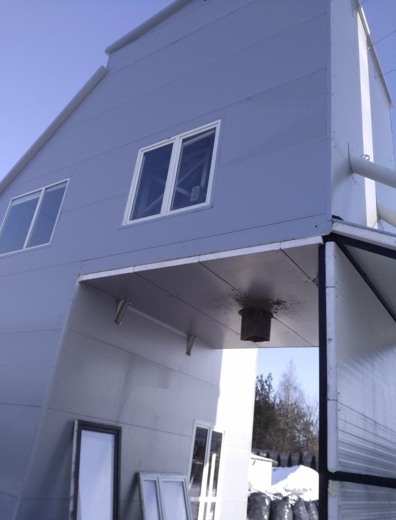 Zewnętrzny widok budowanej hali z paneli warstwowych, z widocznymi oknami i przygotowanymi do montażu oknami na ziemi, w tle zimowy krajobraz.