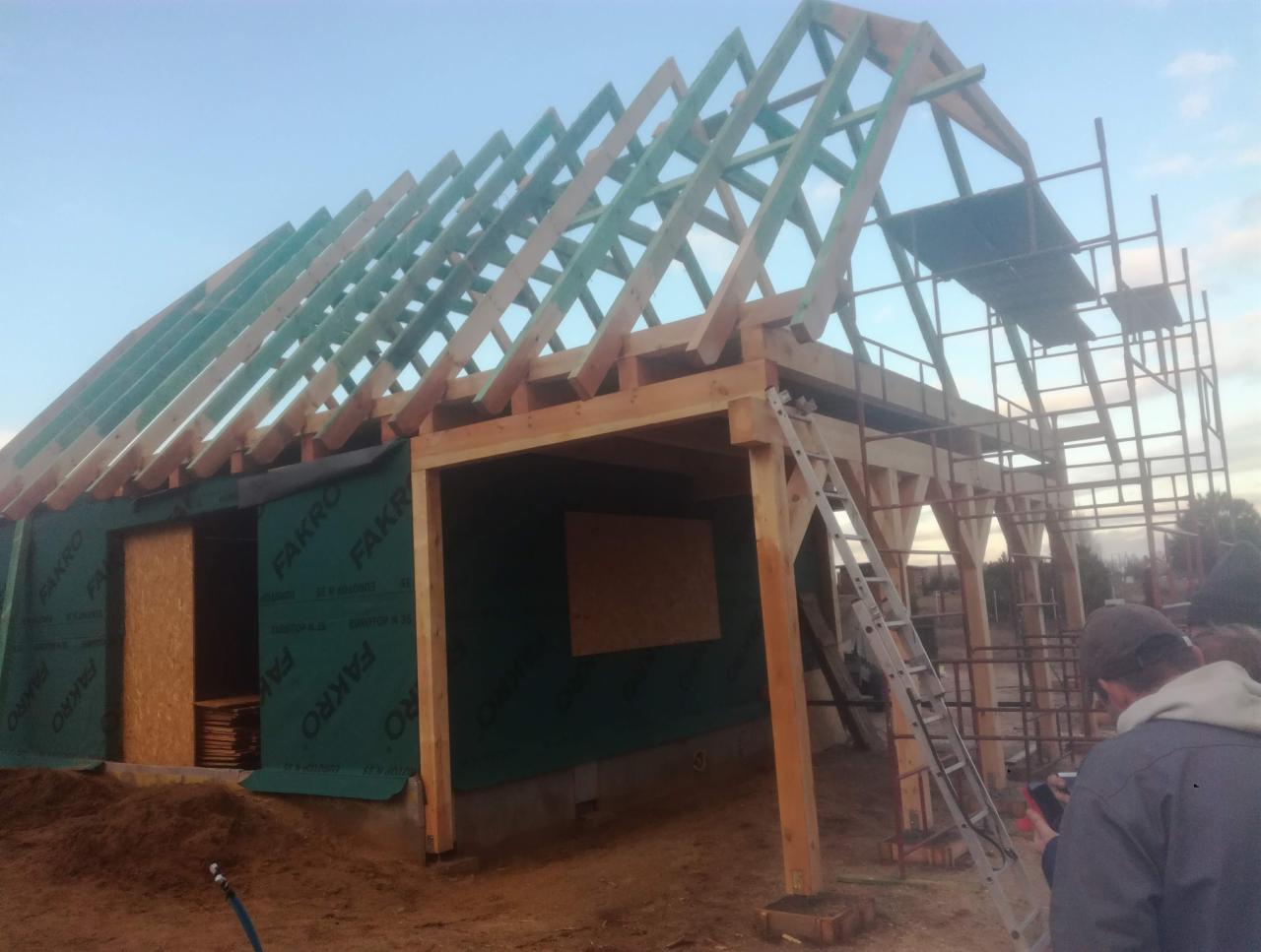 Konstrukcja domu szkieletowego w trakcie budowy, widoczne drewniane elementy nośne, rusztowanie i folia izolacyjna z logo Fakro. W tle błękitne niebo.