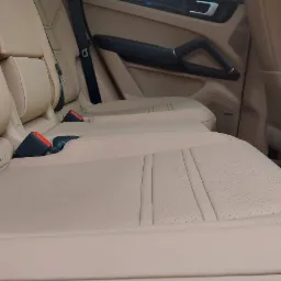 Beżowa skórzana tapicerka tylnych siedzeń luksusowego samochodu, widoczne pasy bezpieczeństwa i kratka wentylacyjna.