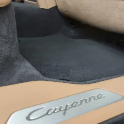 Wnętrze samochodu Porsche Cayenne: czarna welurowa podłoga i beżowe elementy wykończenia, widoczny próg z napisem modelu, oświetlenie wnętrza podkreśla detale.