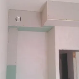 Wnętrze w trakcie montażu konstrukcji z płyt gipsowo-kartonowych, widoczny fragment sufitu podwieszanego z otworem na oświetlenie oraz obudowa ściany, surowe ściany przygotowane do dalszych prac...