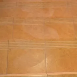 Beżowe płytki na schodach z antypoślizgowymi rowkami, widok z góry.