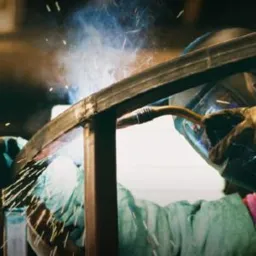 Spawanie metalowej konstrukcji ramowej przez spawacza w hełmie ochronnym, iskry i dym widoczne w miejscu łączenia.