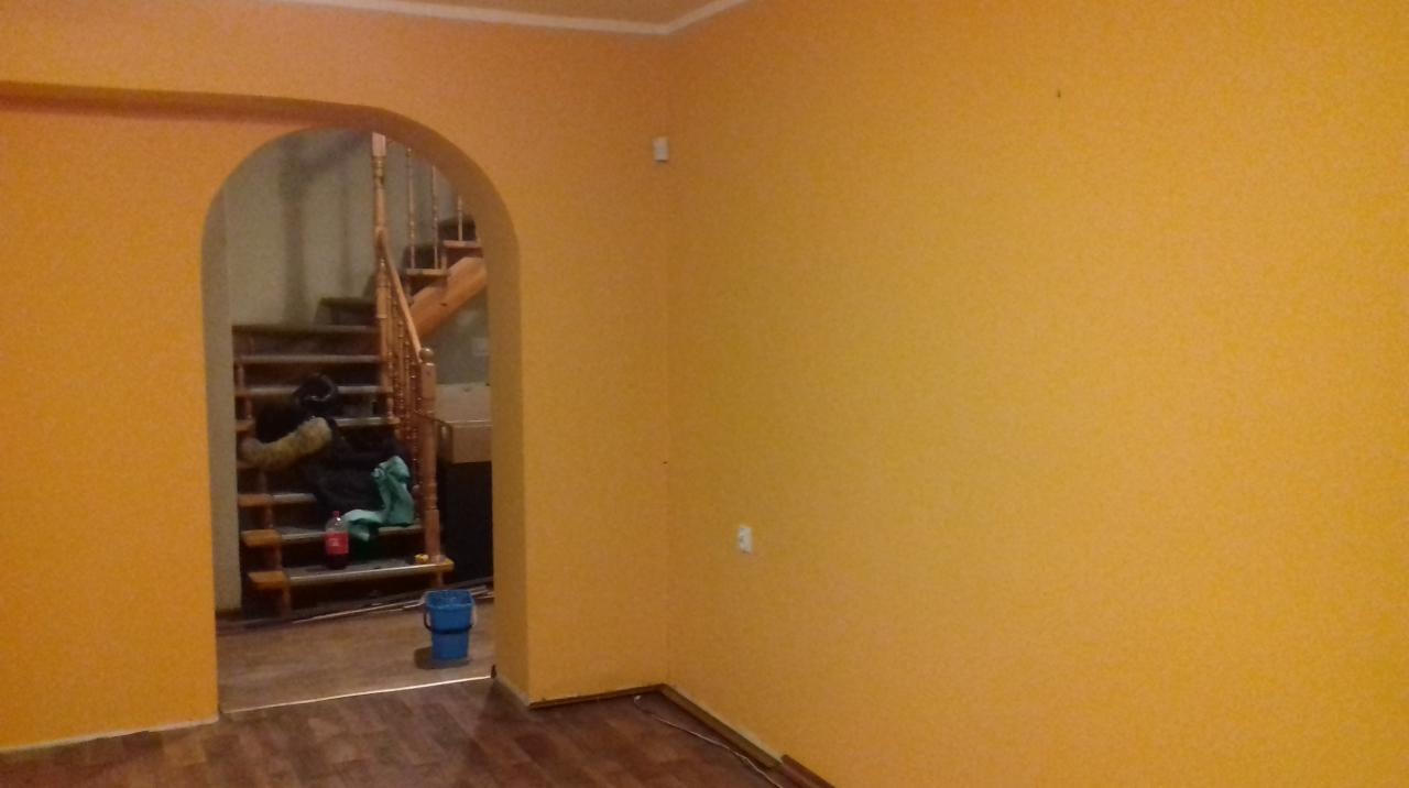 Pomarańczowa ściana po malowaniu z widocznym wejściem do drugiego pomieszczenia, gdzie widać schody, wiadro i butelkę napoju na schodach.