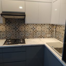 REFIT ADAM KORODY - Nowoczesna kuchnia z białymi szafkami górnymi, szarymi dolnymi, marmurowym blatem i płytkami w stylu retro nad kuchenką gazową.