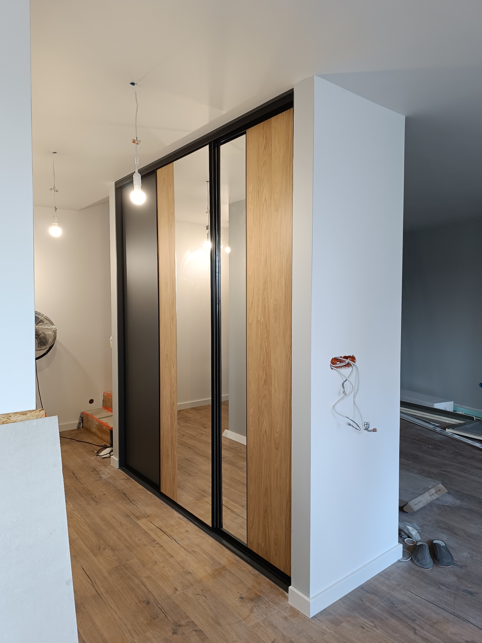 Nowoczesna szafa wnękowa z przesuwnymi drzwiami, z elementami lustrzanymi i drewnopodobnymi, w trakcie montażu w Gliwicach, widoczne niedokończone prace wykończeniowe.