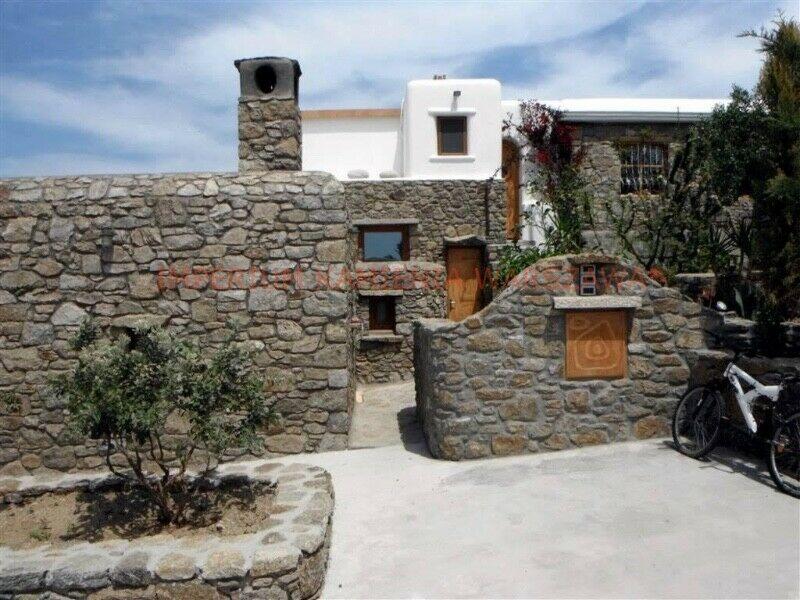 Kamienny dom z kominem, otoczony murem z kamienia i tarasem, z rowerem opartym o ścianę.