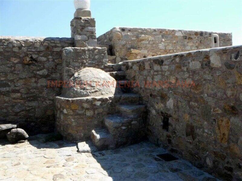 Kamienne schody zewnętrzne i taras z murem oporowym, wykonane z nieregularnych kamieni w odcieniach szarości i beżu, z kominem w tle.