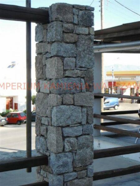 Kamienna kolumna ogrodzeniowa w Piasecznie, wykonana z nieregularnych bloków szarego kamienia, element drewnianego ogrodzenia w tle.