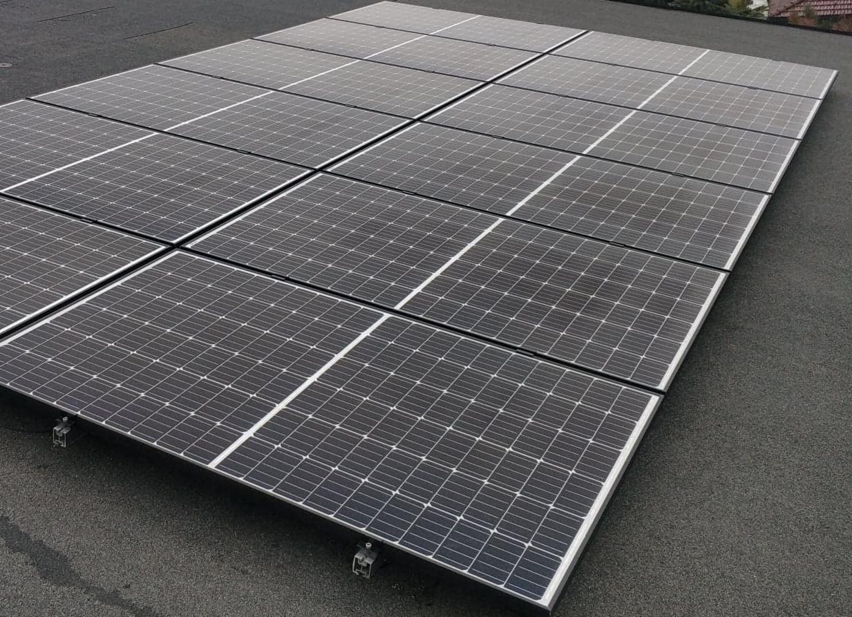 Czarny dach pokryty panelami słonecznymi w układzie prostokątnym, widoczne metalowe mocowania paneli.