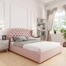 Różowe łóżko tapicerowane z pikowanym zagłówkiem w jasnej sypialni z parkietem w jodełkę, obok szafka nocna z lampką i ramkami.