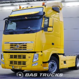 Żółty ciągnik siodłowy Volvo FH z naczepą, sfotografowany z przodu na tle szarej ściany z poziomymi panelami. Widoczna tablica rejestracyjna BX-TD-15.