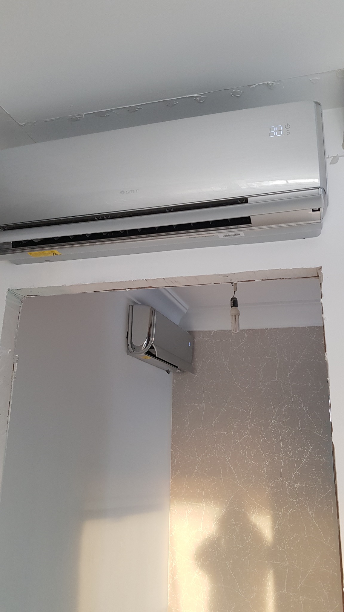 Dwa klimatyzatory marki Gree zamontowane w pomieszczeniu, jeden na suficie, drugi na ścianie, widoczne ślady po remoncie na suficie.