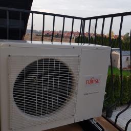 Klima Control - Zewnętrzna jednostka klimatyzacji Fujitsu DC Inverter zamontowana na balkonie z widokiem na osiedle domów i zielone tuje.