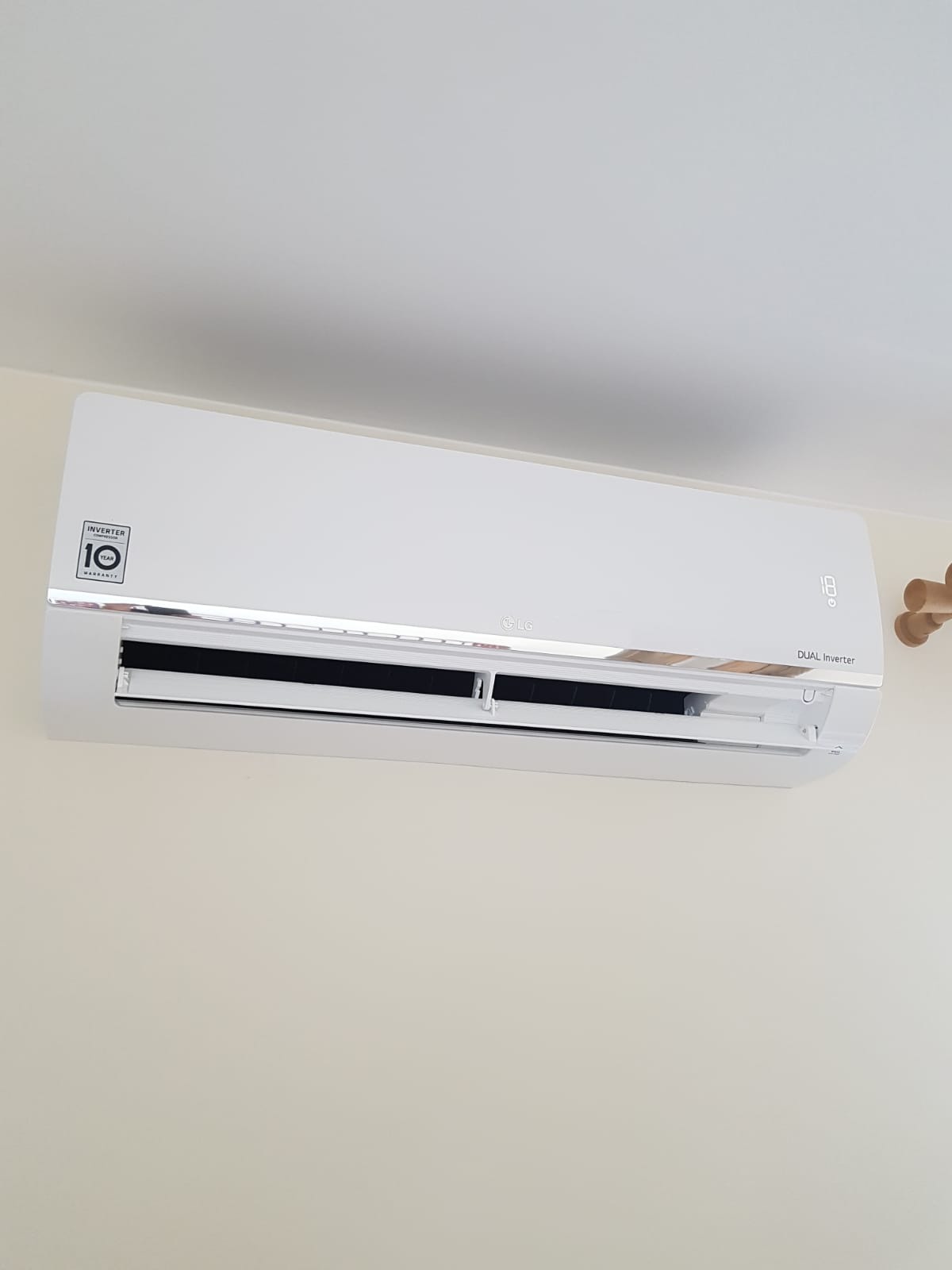 Biała klimatyzacja LG Dual Inverter zamontowana na jasnej ścianie, widoczny wyświetlacz temperatury i naklejka z 10-letnią gwarancją na inwerter.