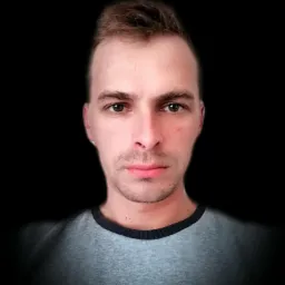 Portret mężczyzny z bliska na czarnym tle, z widoczną drobną zmianą skórną na policzku.