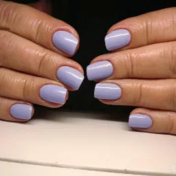 Dłonie z świeżo pomalowanymi paznokciami w odcieniu pastelowego fioletu, ukazujące starannie wykonany manicure hybrydowy o kwadratowym kształcie.