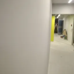 Świeżo pomalowana, jasna ściana korytarza w budynku biurowym, z widocznymi śladami prac malarskich i drabiną w tle.