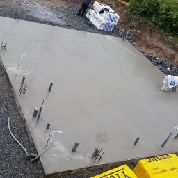 Ata Development - Świeżo wylana, gładka płyta fundamentowa z wystającymi rurami instalacyjnymi i prętami zbrojeniowymi, widok z góry na plac budowy z przygotowanym materiałem izolacyjnym.