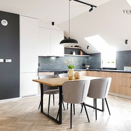 YES4DESIGN Elwira Bowycz-Stryjek - Jasna kuchnia z drewnianymi szafkami, szarym blatem i marmurową ścianą, stół z szarymi krzesłami, parkiet w jodełkę, czarna lampa wisząca i reflektory szynowe.