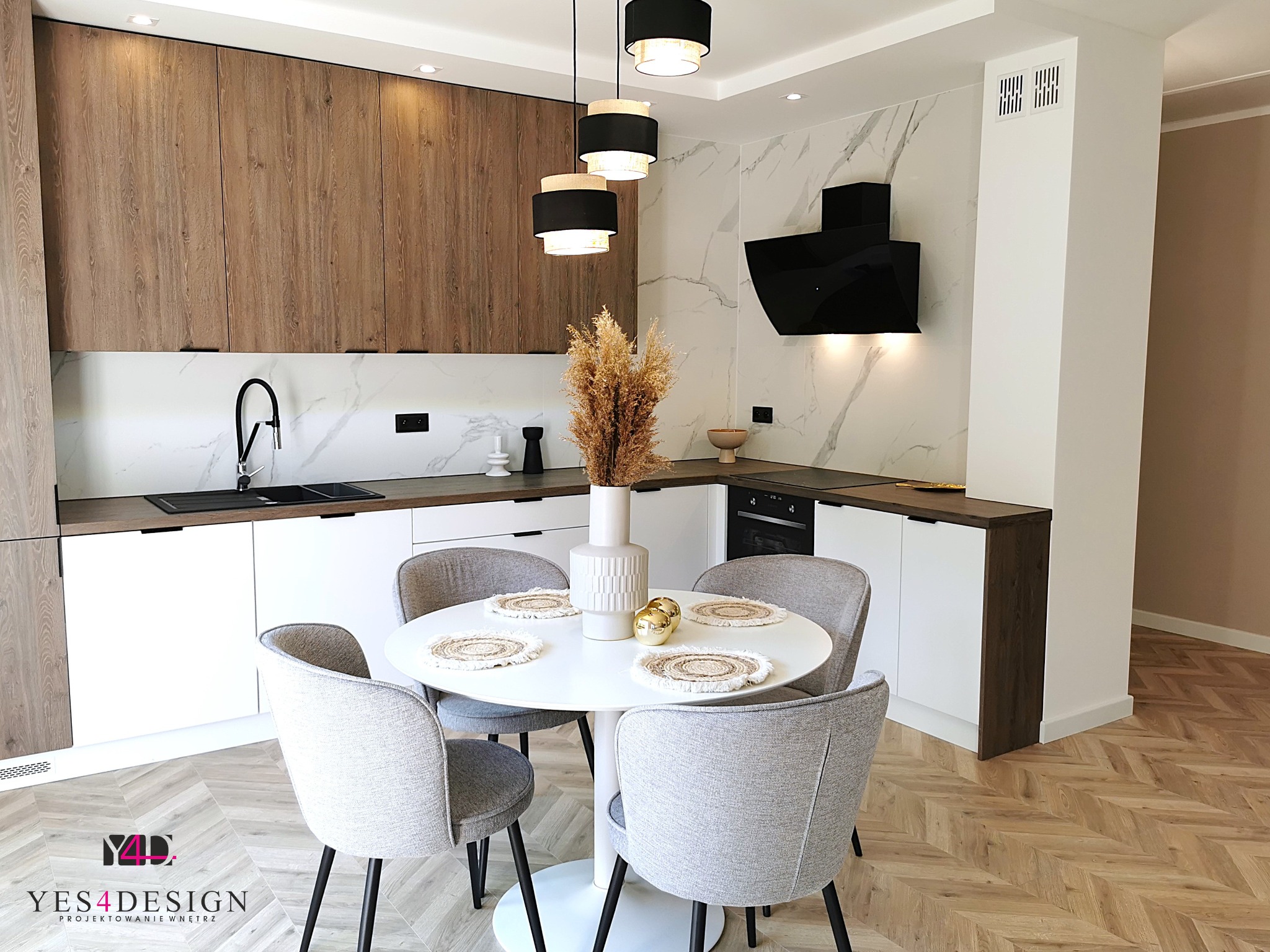 Nowoczesna kuchnia z białymi i drewnianymi szafkami, marmurowym backsplashiem, okrągłym stołem z szarymi krzesłami i parkietem w jodełkę.