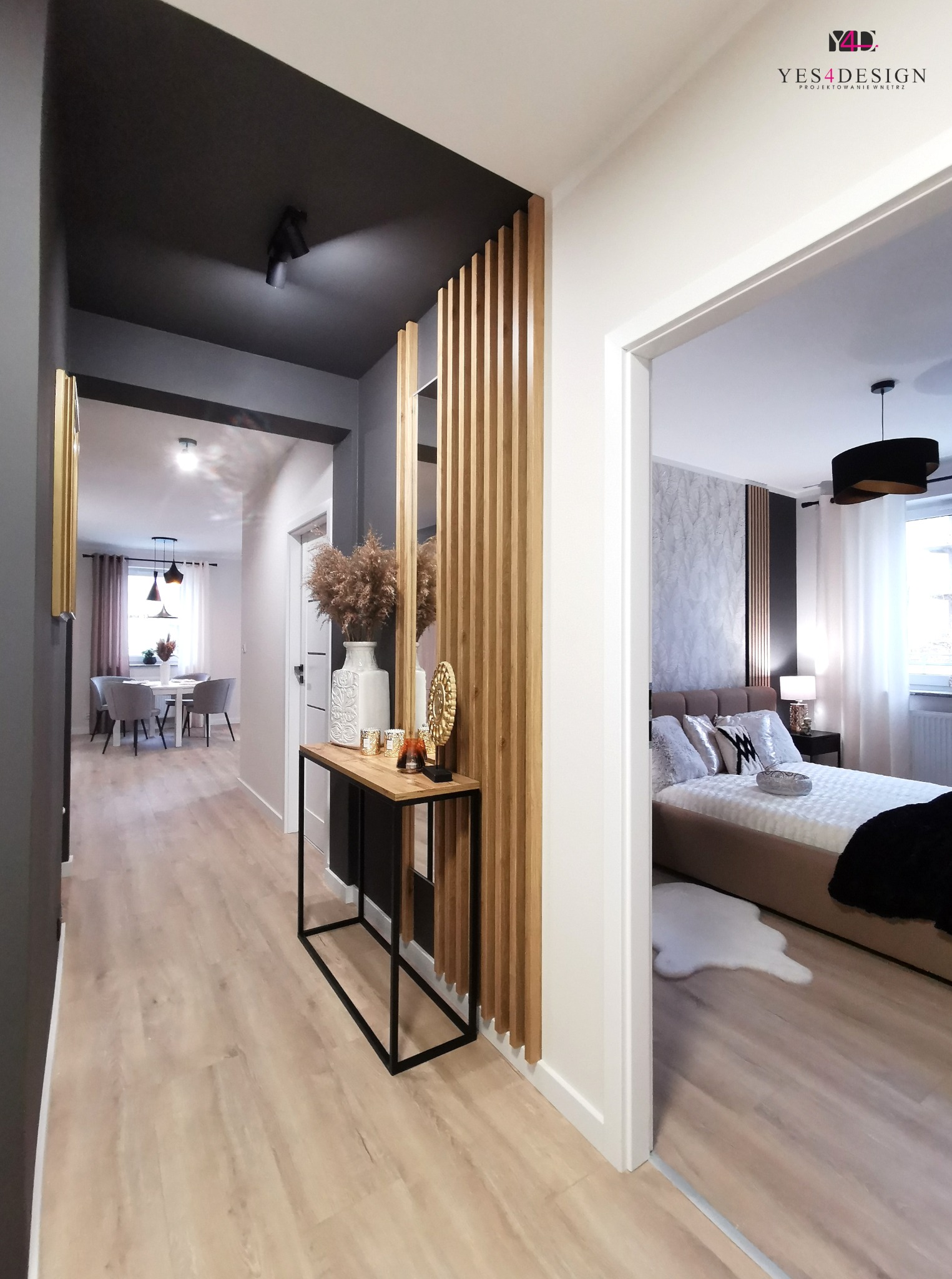 Nowoczesny korytarz z drewnianymi lamelami, konsolą z dekoracjami i widokiem na jadalnię oraz sypialnię z tapetą w liście.