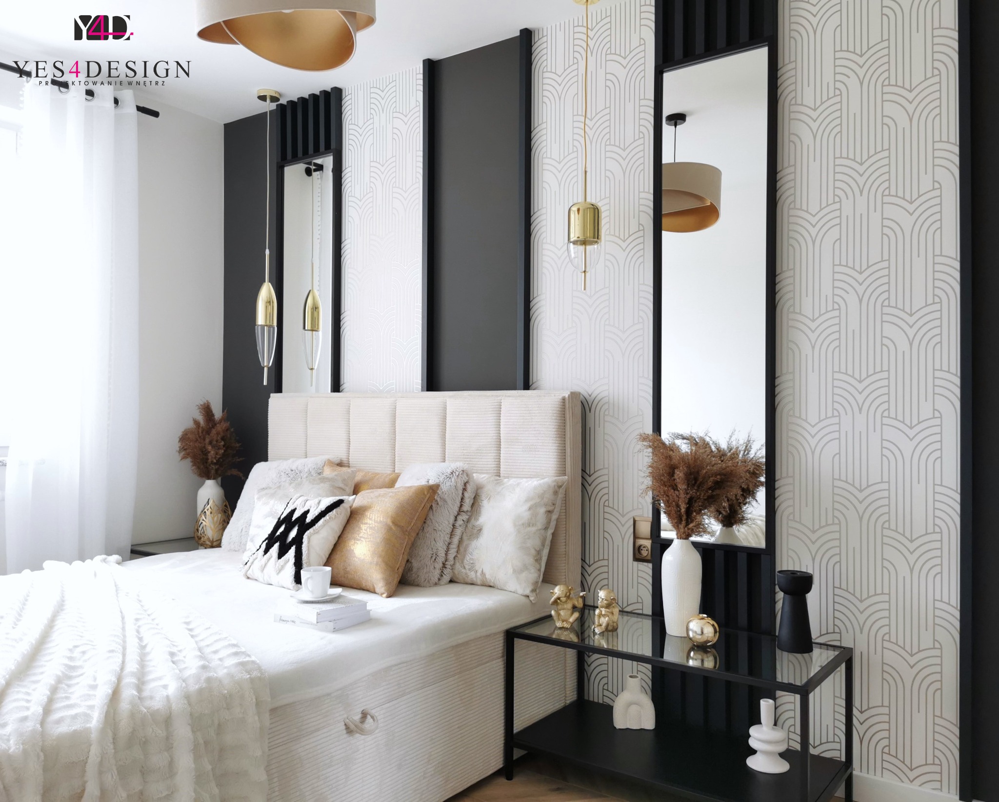 Elegancka sypialnia z beżowym łóżkiem, dekoracyjnymi poduszkami, złotymi lampami wiszącymi i tapetą w geometryczne wzory, uzupełniona czarnymi akcentami i szklanym stolikiem nocnym z dekoracjami.
