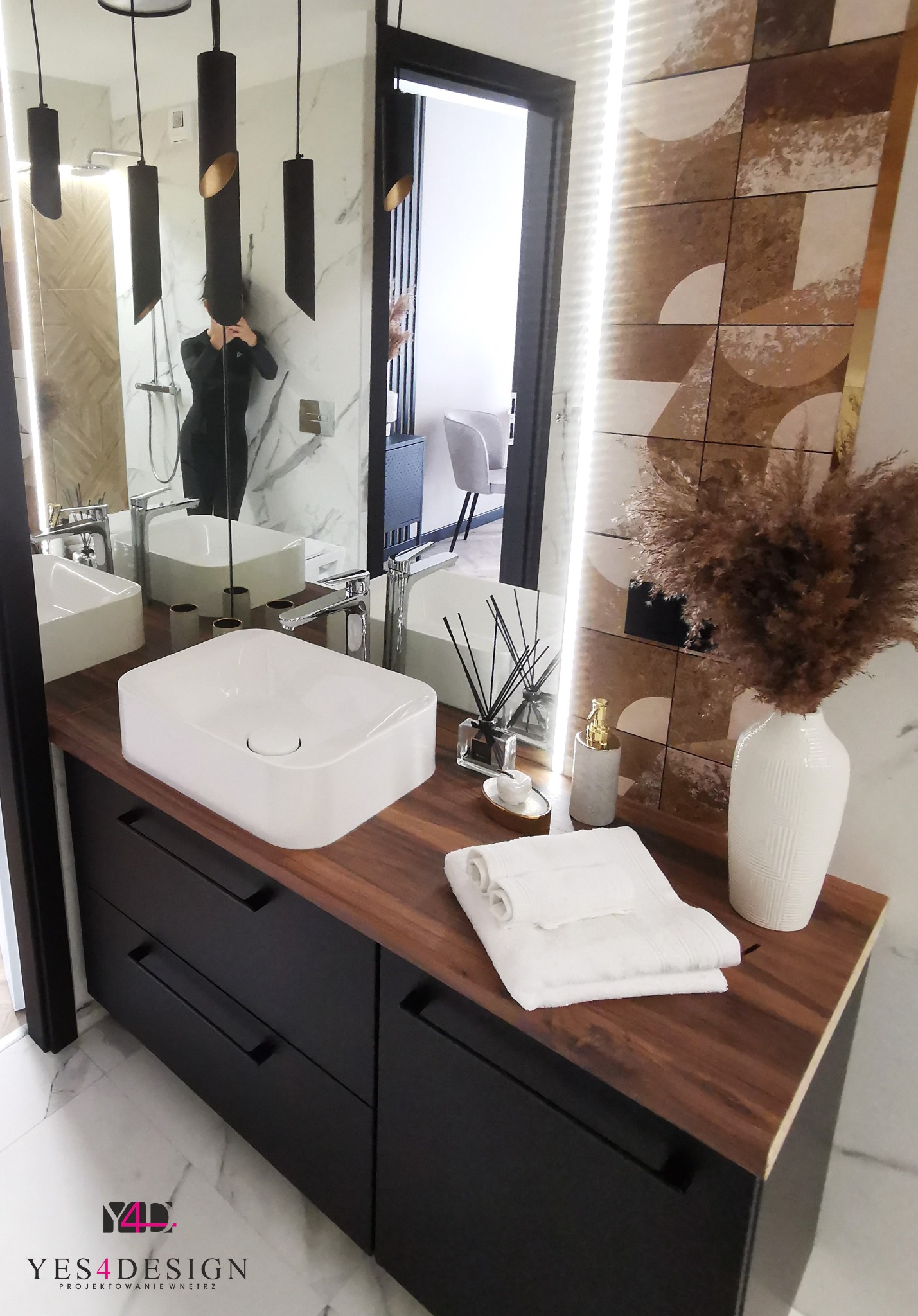 Nowoczesna łazienka w Zielonej Górze z umywalką nablatową o kwadratowym kształcie, czarnymi szafkami z drewnianym blatem, dekoracyjną ścianą z mozaiką i wysoką białą wazą z suchymi trawami.
