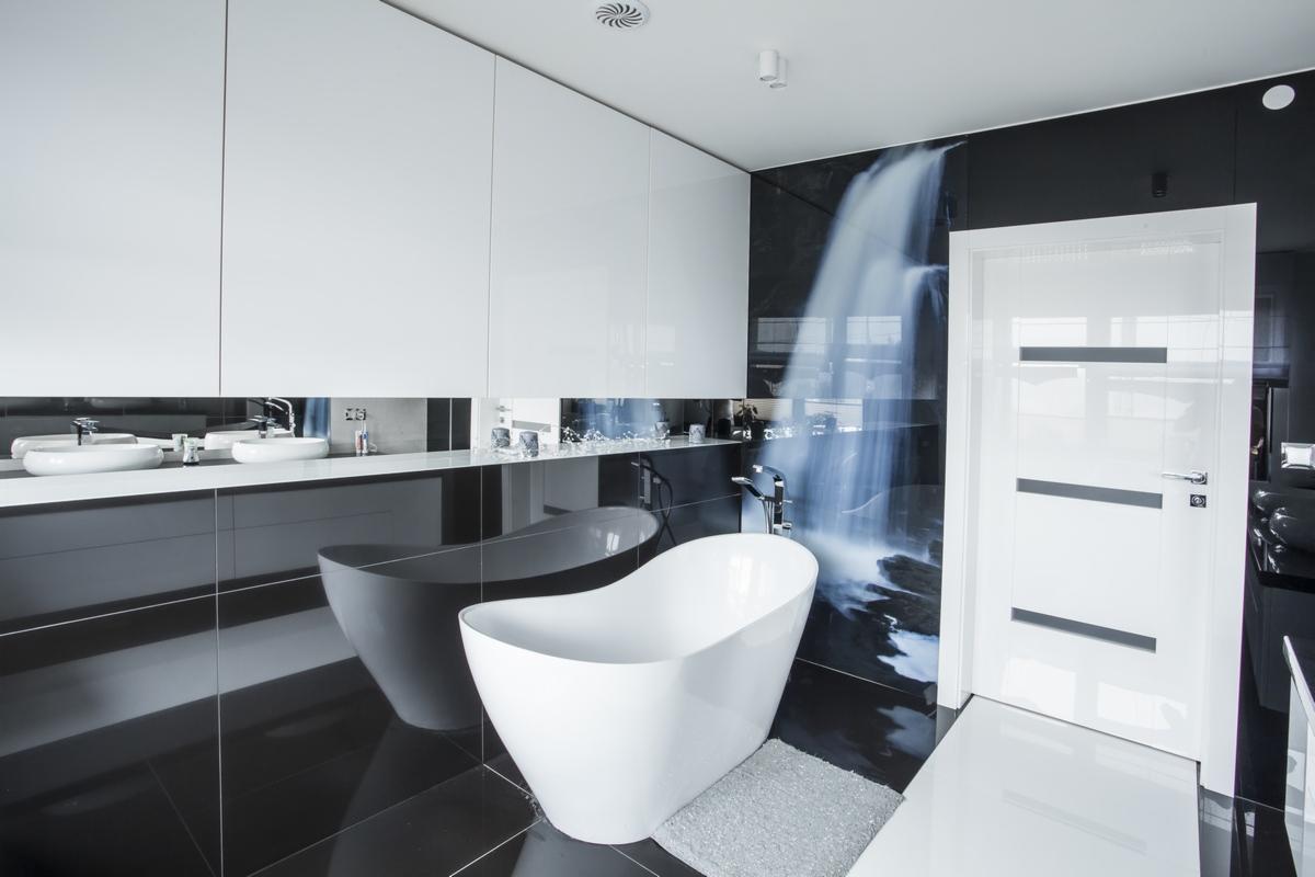 Nowoczesna łazienka w czerni i bieli z wolnostojącą wanną, szafkami z połyskiem i fototapetą z motywem wodospadu.