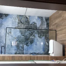 Wykończona łazienka z kabiną prysznicową typu walk-in, wyłożona płytkami imitującymi marmur w odcieniach błękitu i szarości oraz drewnopodobnymi płytkami na ścianie bocznej, widok z zewnątrz przez...