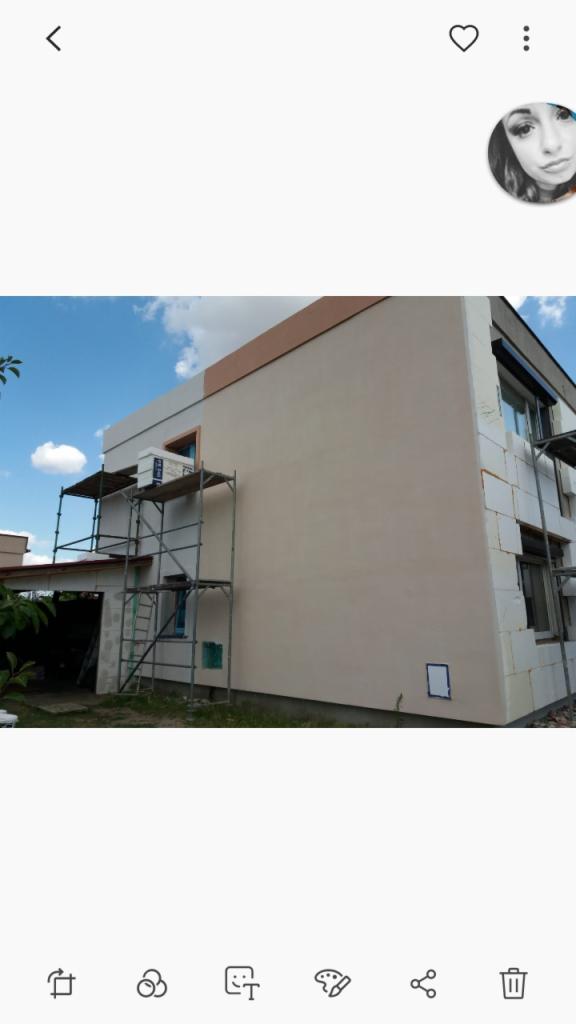 Dwupiętrowy dom w trakcie ocieplania, widoczne rusztowania i częściowo ocieplona elewacja z białym styropianem, obok garaż.