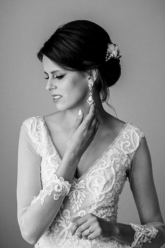 Panna młoda w koronkowej sukni, dotyka kolczyka, profil twarzy, czarno-białe zdjęcie.