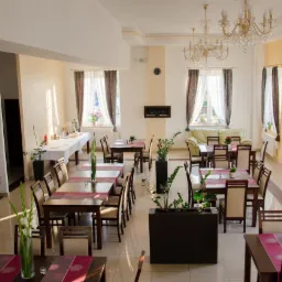 Jasna sala bankietowa z nakrytymi stołami, dekoracjami kwiatowymi i żyrandolami, przygotowana na przyjęcie.