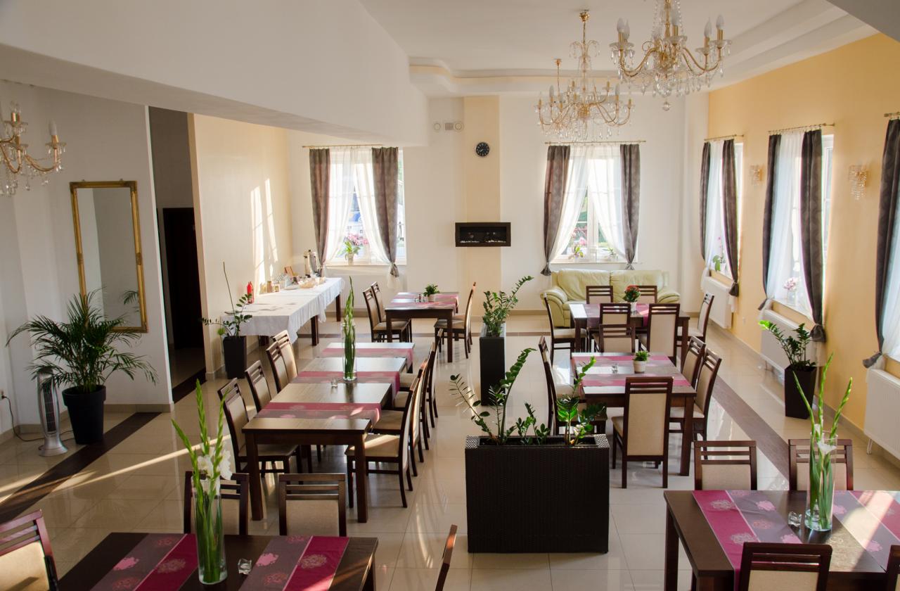 Jasna sala bankietowa z nakrytymi stołami, dekoracjami kwiatowymi i żyrandolami, przygotowana na przyjęcie.