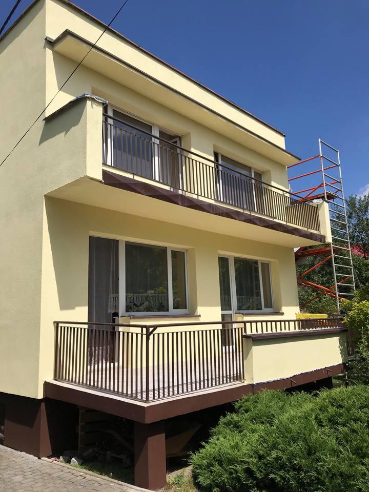 Dwupiętrowy dom z balkonami po odświeżeniu elewacji w odcieniach żółci, z widocznym rusztowaniem z boku budynku.