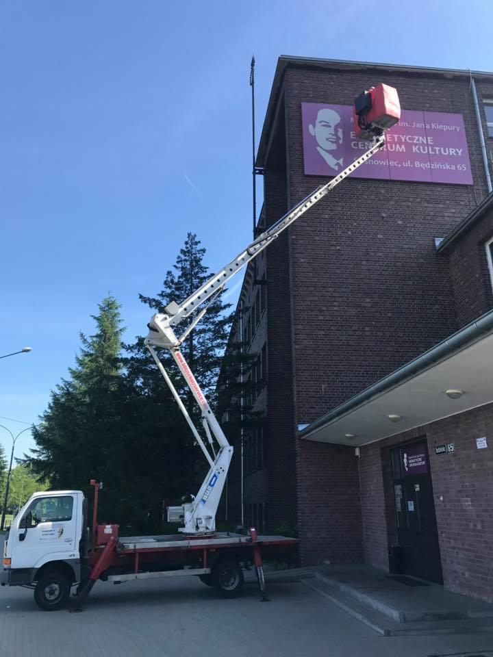 Podnośnik koszowy na pojeździe ustawiony przed budynkiem z cegły z szyldem 'Etnetyczne Centrum Kultury im. Jana Kiepury' w Sosnowcu, ul. Będzińska 65.