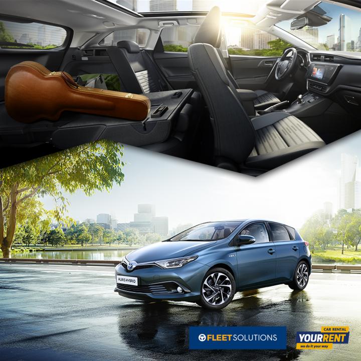 Niebieski hatchback Auris Hybrid na tle parku i miasta, wnętrze z futerałem na gitarę na tylnym siedzeniu, widok z panoramicznego dachu.