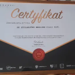 Oprawiony certyfikat firmy PK Stolarstwo Meblowe Piotr Kr&oacute;l, potwierdzający wsp&oacute;łpracę z Kaczmarski Group, z datą 2022, prezentowany z bliska na tle wzorzystej powierzchni.