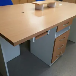 Biurko z jasnego drewna z szufladami i wysuwaną półką na klawiaturę, widok z boku, na podłodze leżą kable.