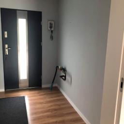 Pk Stolarstwo Meblowe - Nowoczesna, grafitowa dwuskrzydłowa drzwi wejściowe z przeszkleniem, widok na przedpokój z panelami podłogowymi, szarą ścianą i wystającym licznikiem wody.