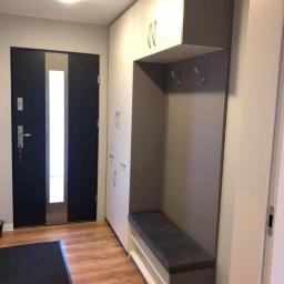 Pk Stolarstwo Meblowe - Nowoczesny przedpokój z zabudową meblową w odcieniach szarości i bieli, obejmującą szafy, szafki z uchwytami oraz wnękę z siedziskiem i wieszakami, uzupełniony o czarne drzwi wejściowe...