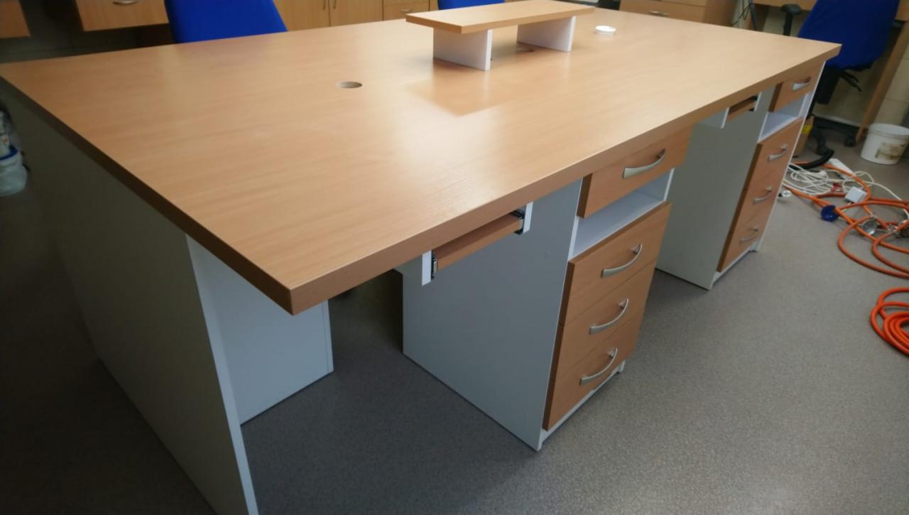 Biurko z jasnego drewna z szufladami i wysuwaną półką na klawiaturę, widok z boku, na podłodze leżą kable.