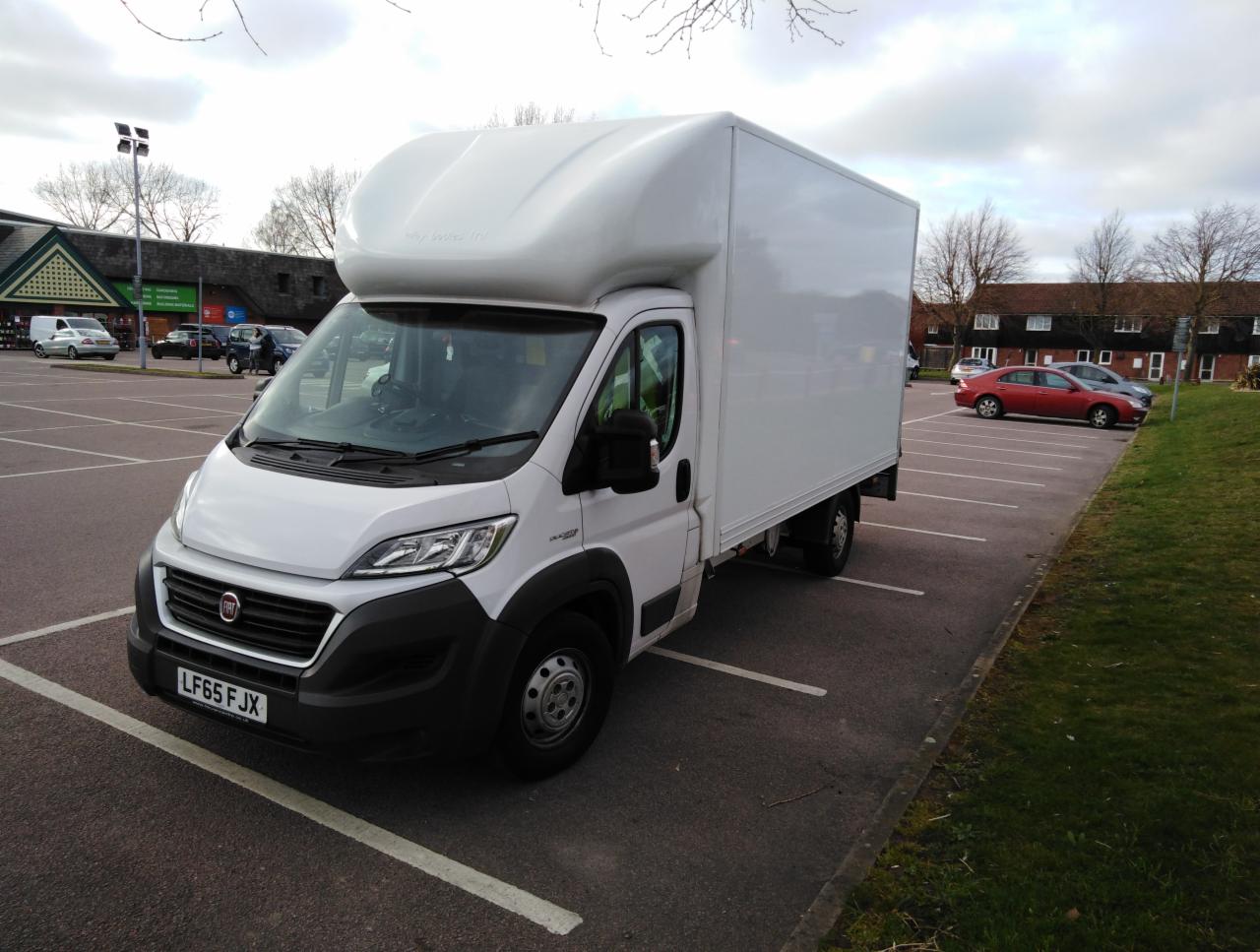 Biała furgonetka dostawcza z wysoką kabiną na parkingu, widoczna tablica rejestracyjna LF65 FJX.