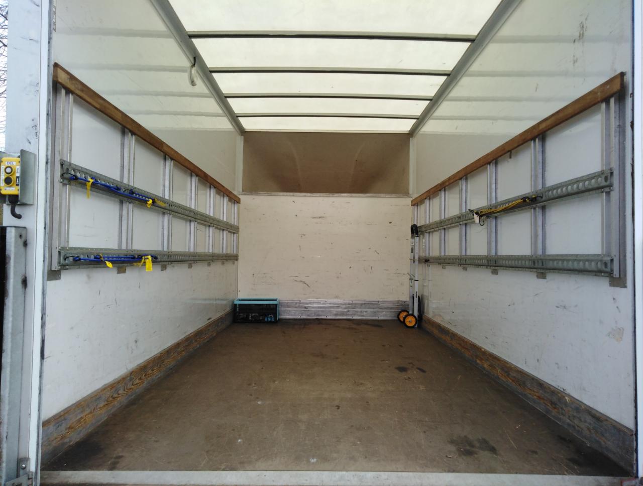 Pusta przestrzeń ładunkowa pojazdu do transportu, widoczne zabezpieczenia ładunku na ścianach, lekko zabrudzona podłoga i oświetlenie sufitowe.