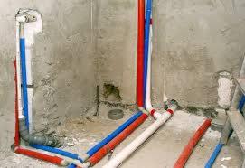 Wnętrze w trakcie remontu z widocznymi rurami instalacji wodnej w kolorach niebieskim i czerwonym, prowadzone wzdłuż surowych, otynkowanych ścian. Fragment drabiny w prawym dolnym rogu.