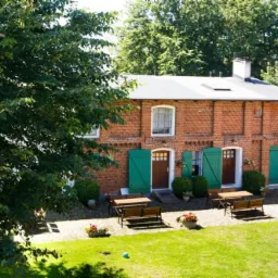 Dwukondygnacyjny budynek z czerwonej cegły z zielonymi okiennicami, widok z zewnątrz na zadbany trawnik i meble ogrodowe.