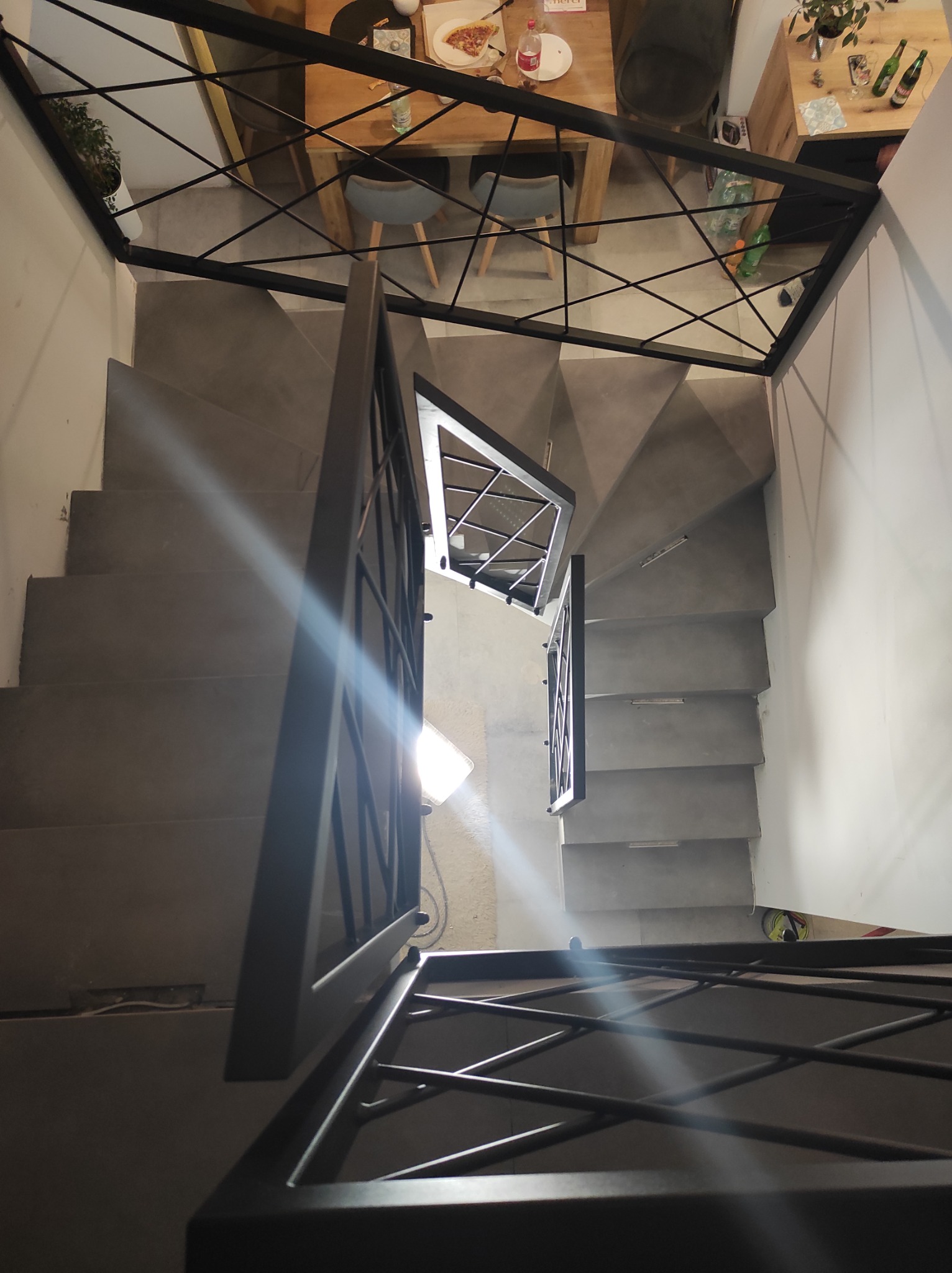 Schody betonowe z czarną, metalową konstrukcją zabezpieczającą, widok z góry, w tle stół z resztkami pizzy.