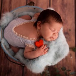 Aleksandra Lauda Fotografia - Śpiący noworodek w błękitnym ubranku, ułożony w metalowym wiaderku wyłożonym futerkiem, z małym czerwonym serduszkiem w dłoni.