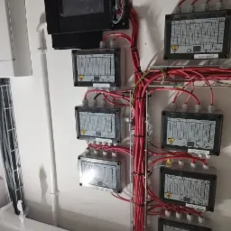 Rozdzielnica elektryczna z podłączonymi przewodami, widoczne oznaczenia na obudowach i kable ułożone w korytku.